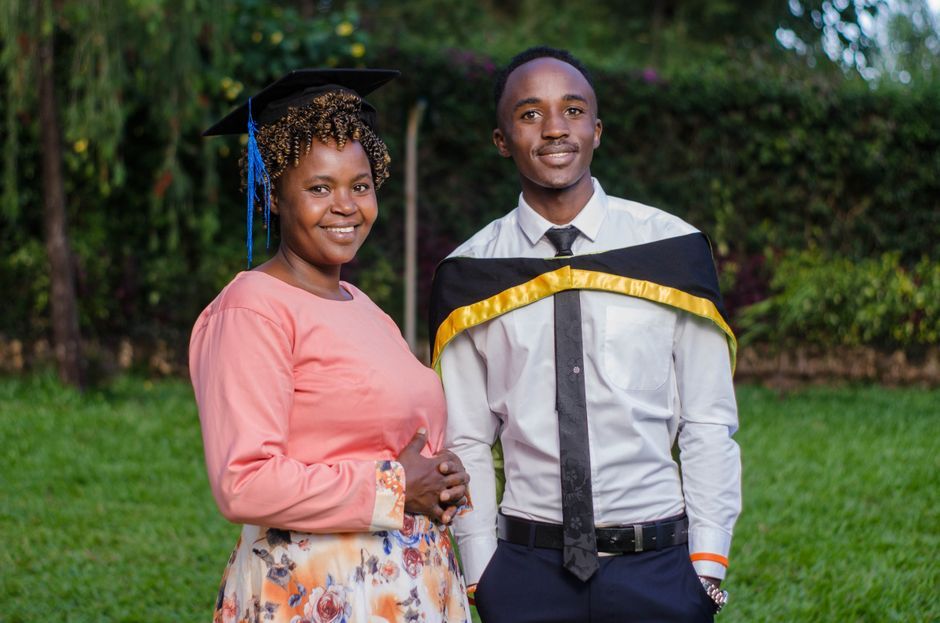Proud mother and son in graduation attire smiling in a garden setting.